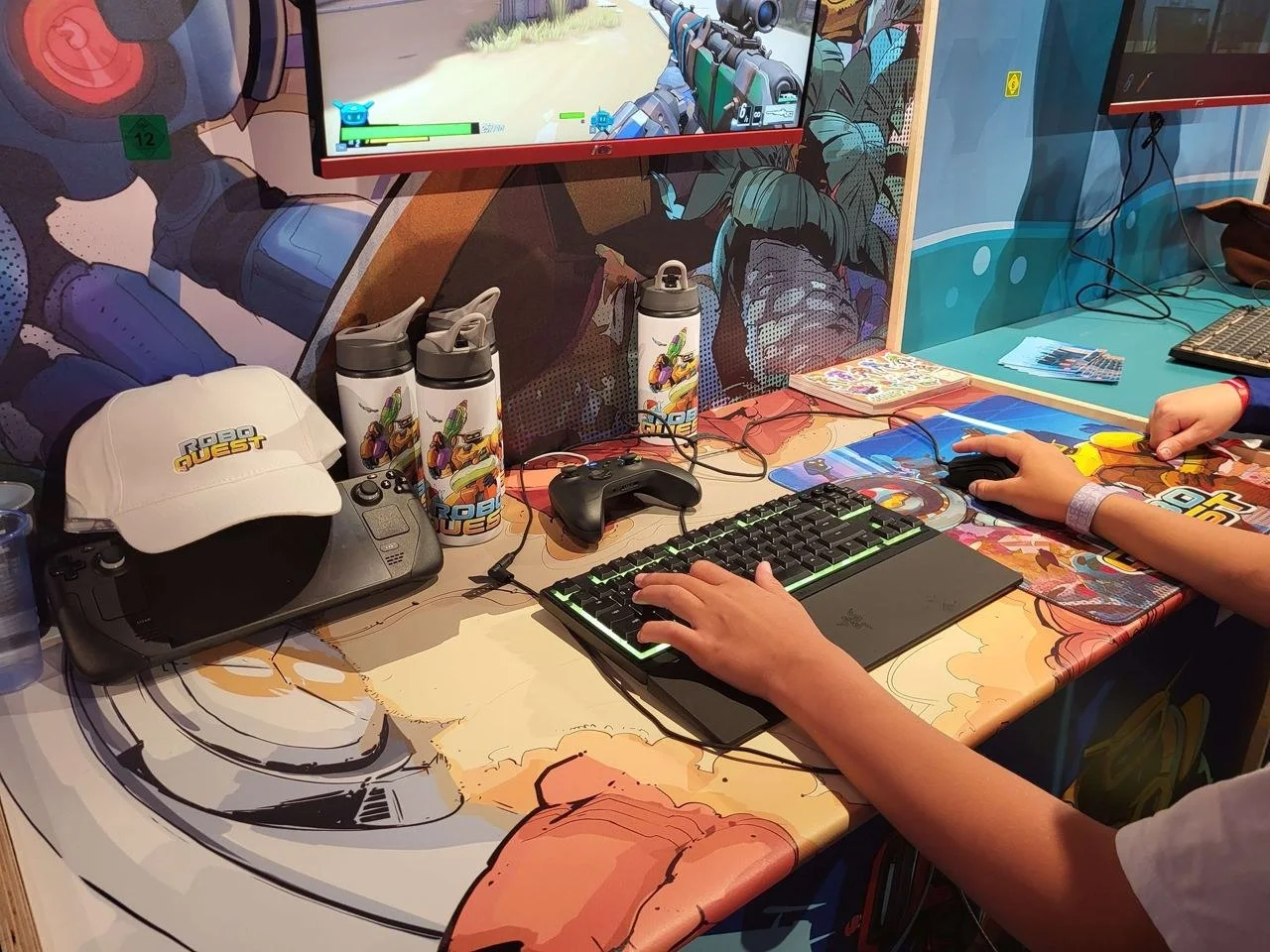Robo Quest gaming merchandise with caps and drink bottles at a gaming station